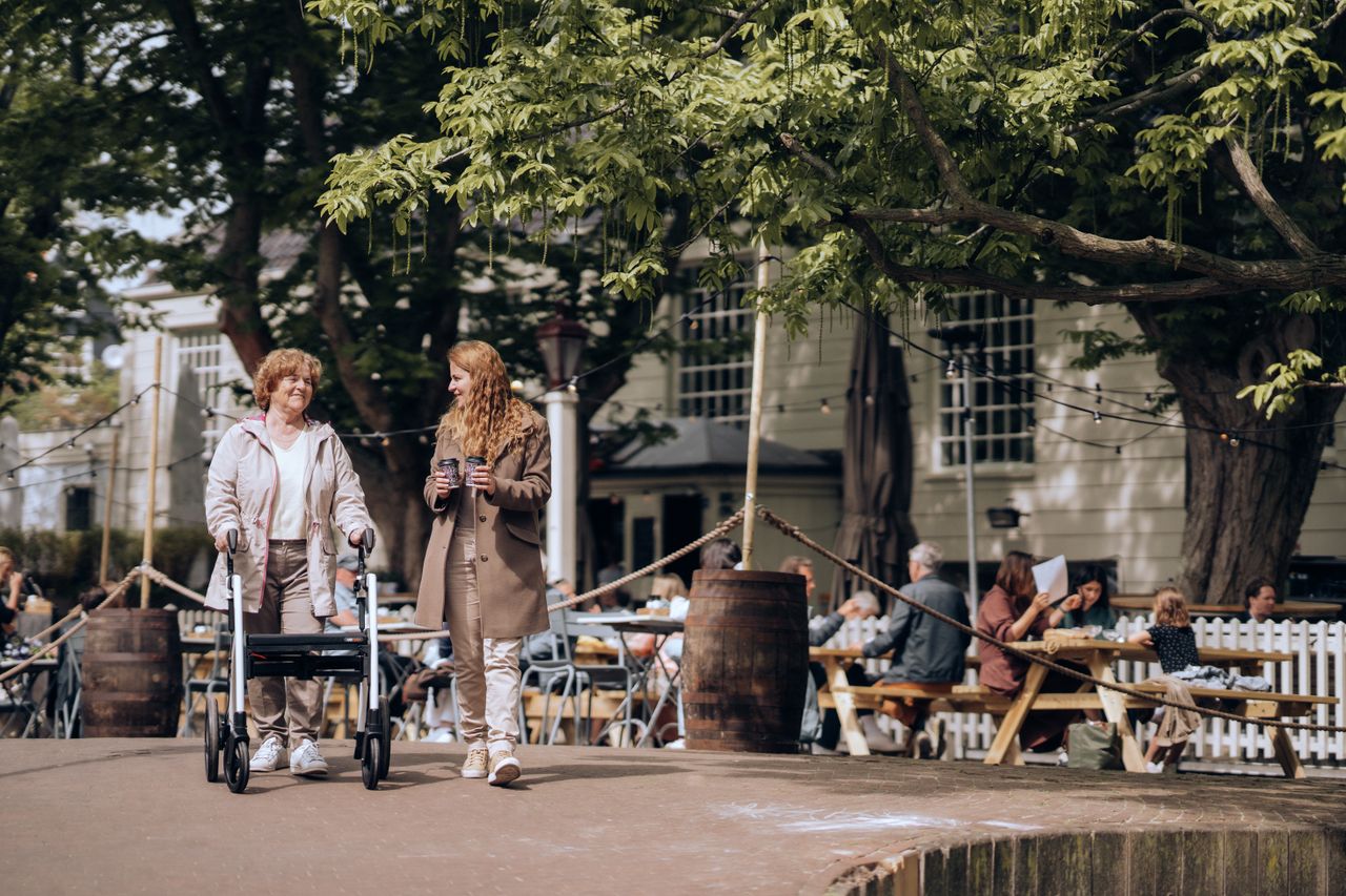 The Art of Drawing Readers In: Your attractive post title goes here Elderly woman with walker and young companion strolling in a lively Amsterdam neighborhood.