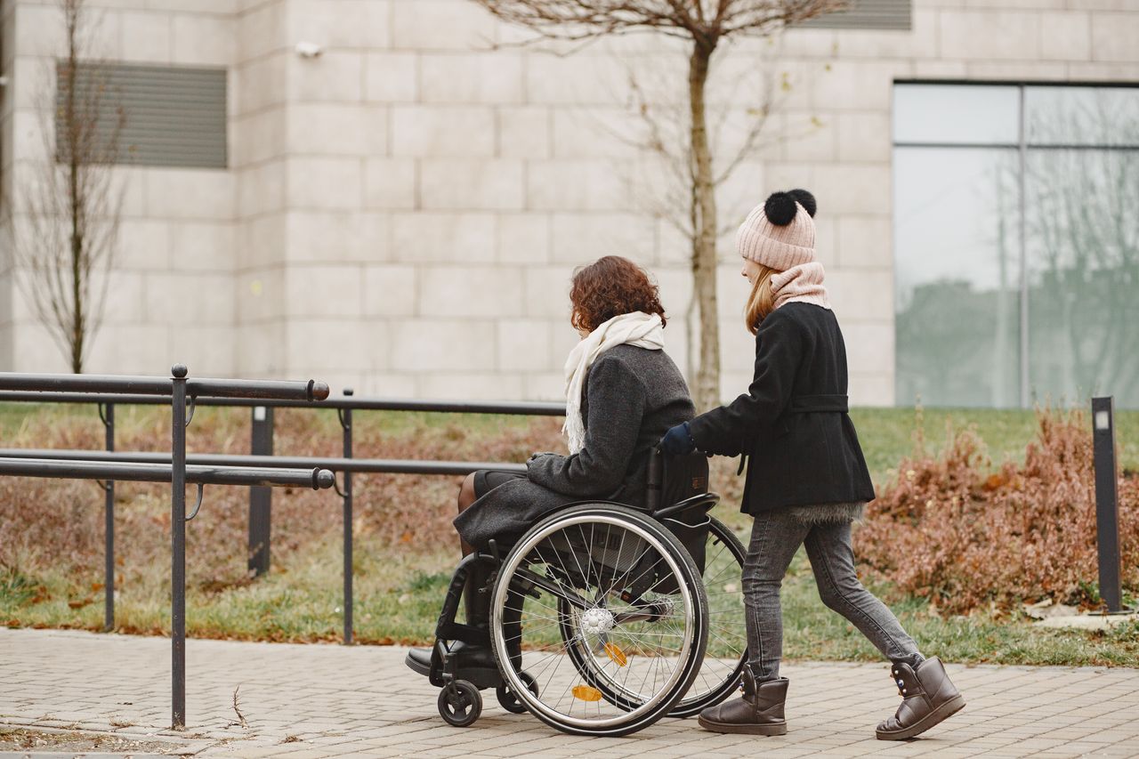 Crafting Captivating Headlines: Your awesome post title goes here A young girl helps a woman in a wheelchair on a sidewalk, showing care and support.